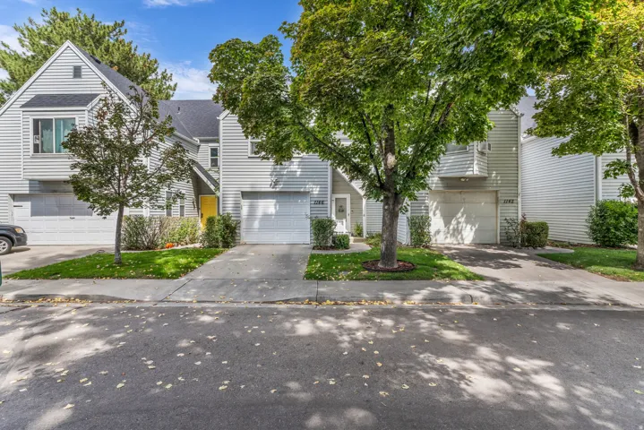 Townhome exterior featuring horizontal siding, attached garage, concrete driveway, and mature landscaping