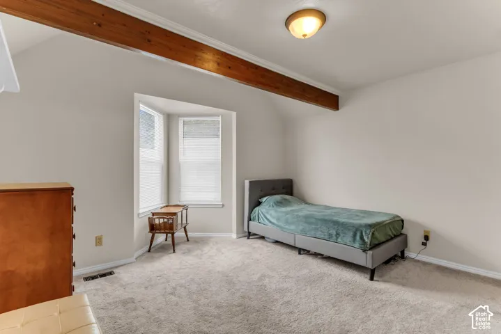 Vaulted ceiling with exposed wood beam, bay window, light neutral wall color, and carpeted flooring
