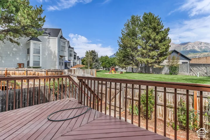 Wood-finish deck with railing, offering a communal green space with mature trees and mountain backdrop