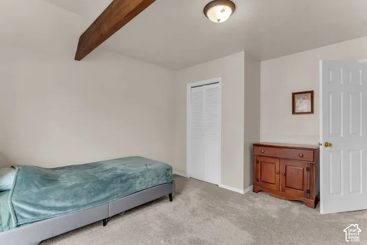 Vaulted ceiling with an exposed wood beam, recessed lighting, neutral tone walls, and carpet flooring