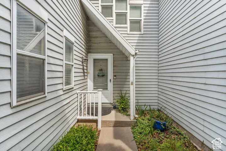 Covered entryway with a white storm door, concrete walkway, and white railing