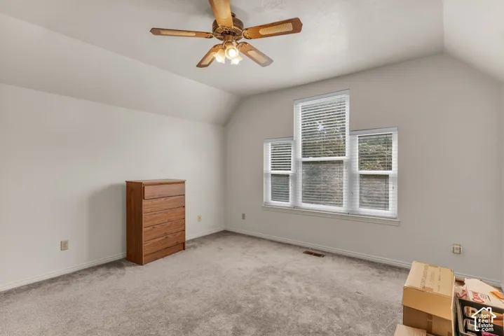 Vaulted ceiling with a ceiling fan, light gray carpet, and three windows with horizontal blinds