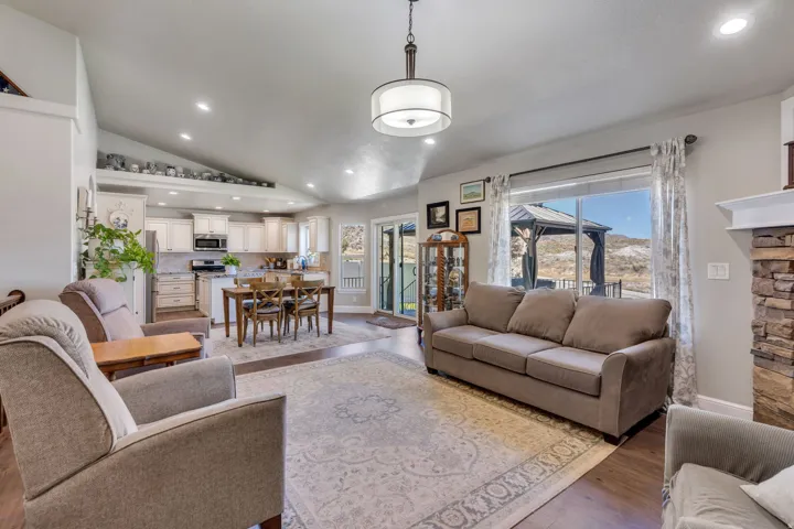 Vaulted ceilings with recessed lighting, kitchen with white cabinetry, wood-finish flooring, stone-clad fireplace, and large windows