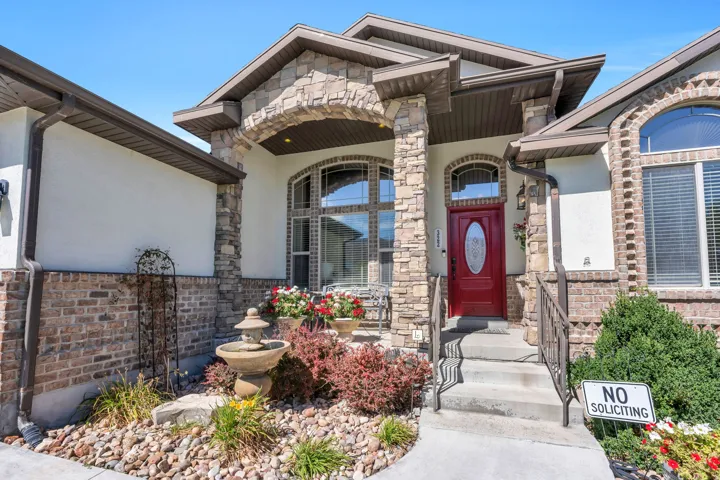 Stucco and brick exterior with stone accents, a deep red entry door, arched windows, and a concrete pathway leading to the entrance