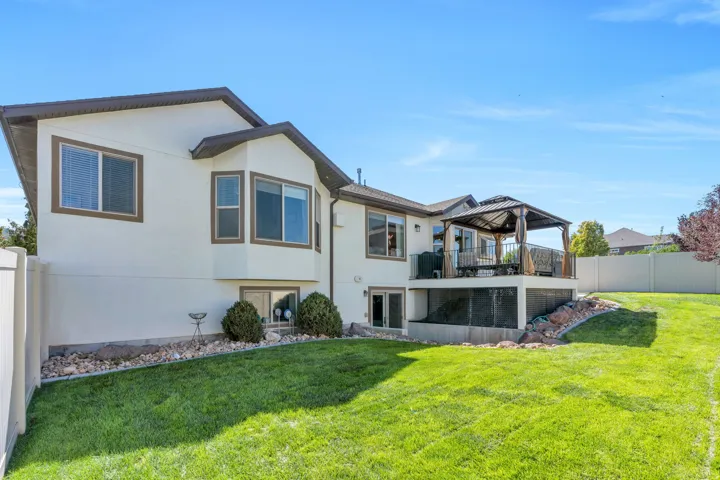 Expansive backyard featuring a manicured lawn, a raised deck with a gazebo, and a lower-level patio with direct outdoor access