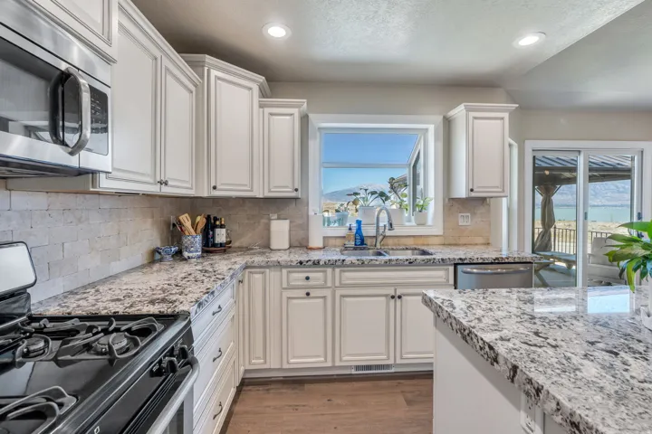 White cabinetry with crown molding, stainless steel appliances, stone slab countertops, tiled backsplash, and wood-finish flooring