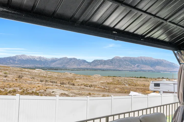Covered patio with metal roof, white privacy fence, and mountain scenery