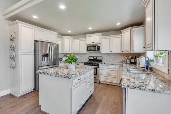 Kitchen featuring white cabinetry, granite countertops, stainless steel appliances, a center island with storage, and wood-finish flooring