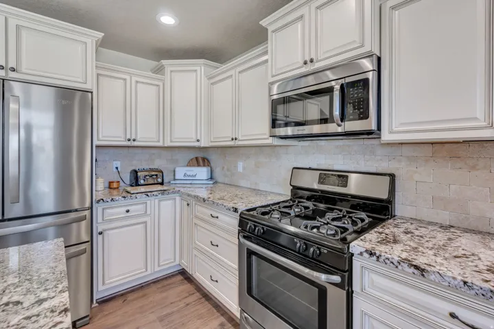 White cabinetry, stainless steel appliances, granite countertops, tile backsplash, and wood-finish flooring