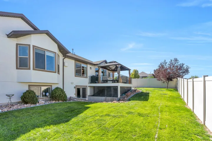 Expansive lawn with a white privacy fence, multi-level exterior, upper-level deck with a gazebo, and lower-level walkout access