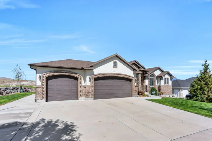 Stucco and brick exterior with arched garage doors, a concrete driveway, and a sloped lawn