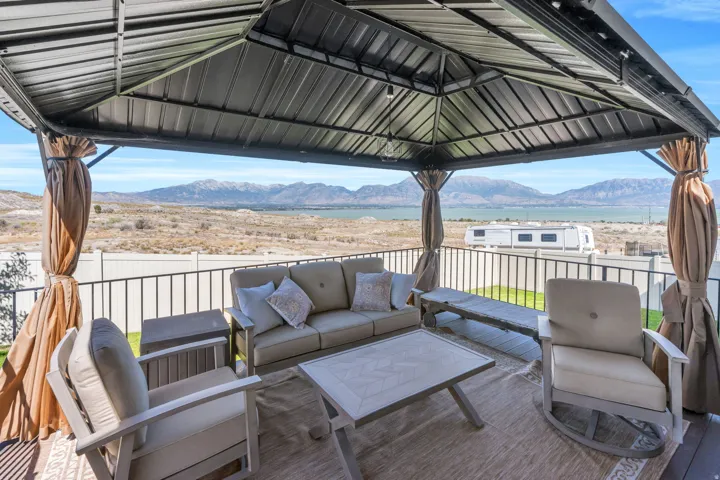 Covered patio with a metal gazebo roof, privacy curtains, and a metal railing overlooking a body of water and distant mountains