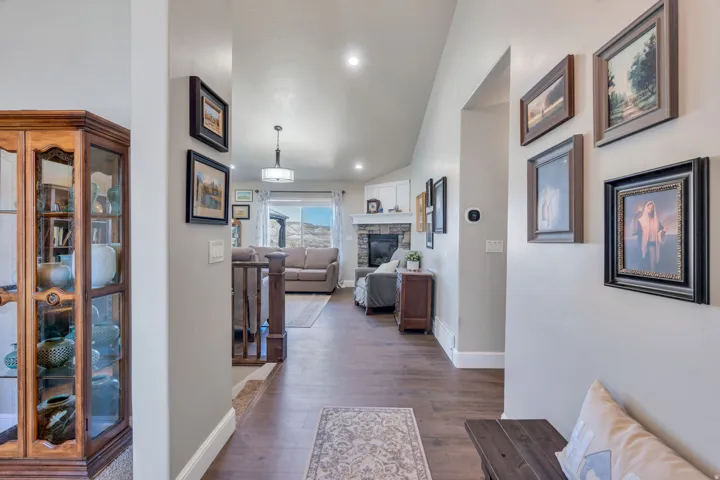 Vaulted ceilings with recessed lighting, wood-finish flooring, staircase with wood railing, and a stone fireplace with a white mantel