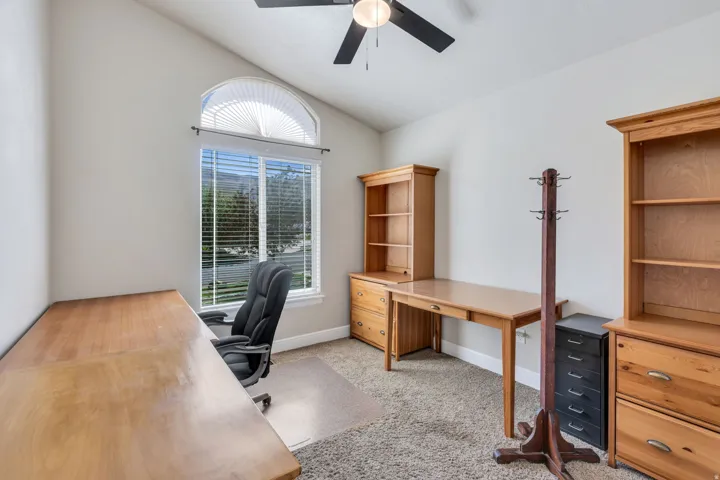 Vaulted ceiling, arched transom window, ceiling fan, and carpeted flooring