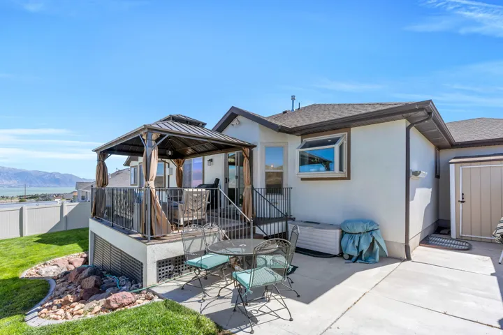Expansive concrete patio with a covered deck featuring a metal gazebo, black metal railing, and direct access to the interior via a glass sliding door