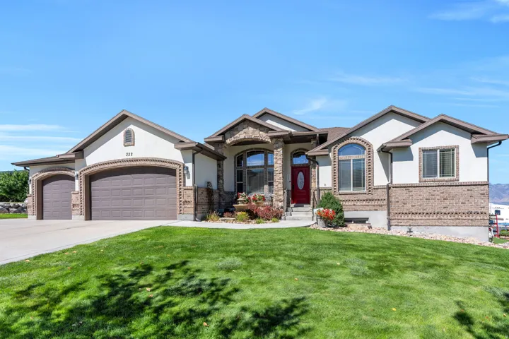 Stucco and brick exterior with stone accents, a three-car garage, arched windows, and a red entry door