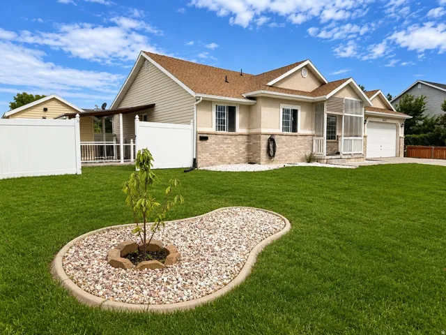 Expansive front lawn with a decorative rock garden, vinyl fencing, and a covered back patio