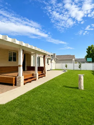 Expansive backyard featuring a large wood deck with pergola, stone-clad columns, a paved patio area, and a lush green lawn