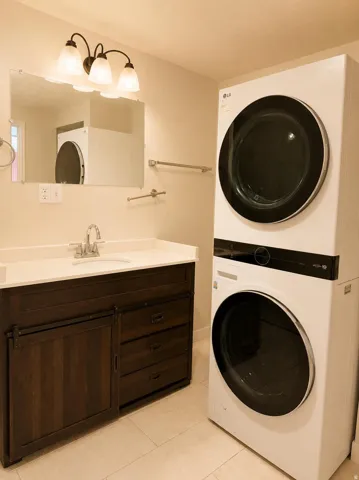 Integrated laundry appliances, dark wood-finish vanity with sliding door, white countertop, and light tile flooring