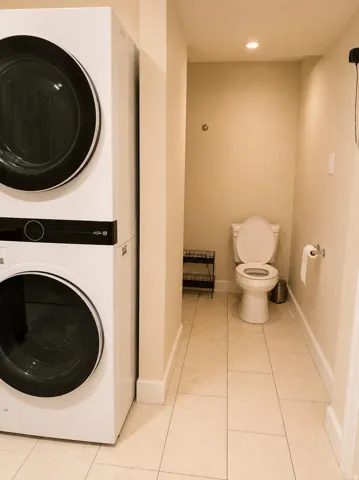 Stacked laundry appliances, recessed ceiling lighting, tile flooring, and a white toilet