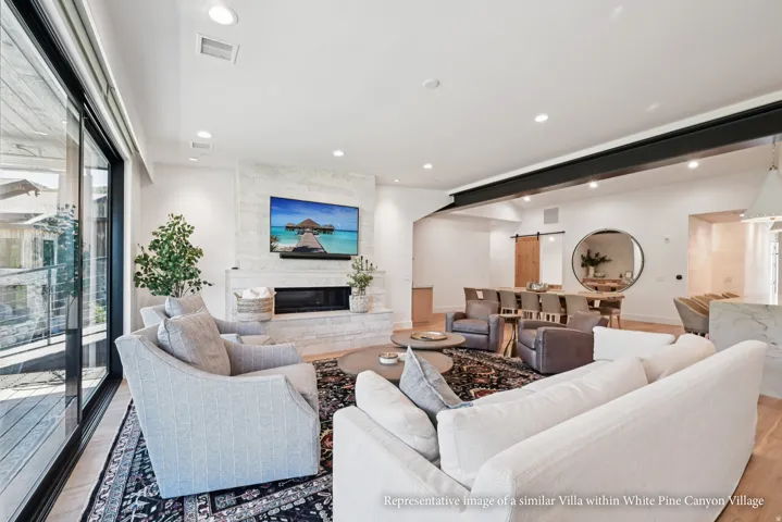 Spacious living area featuring a stone-clad fireplace, large sliding glass doors, recessed lighting, and wood-finish flooring