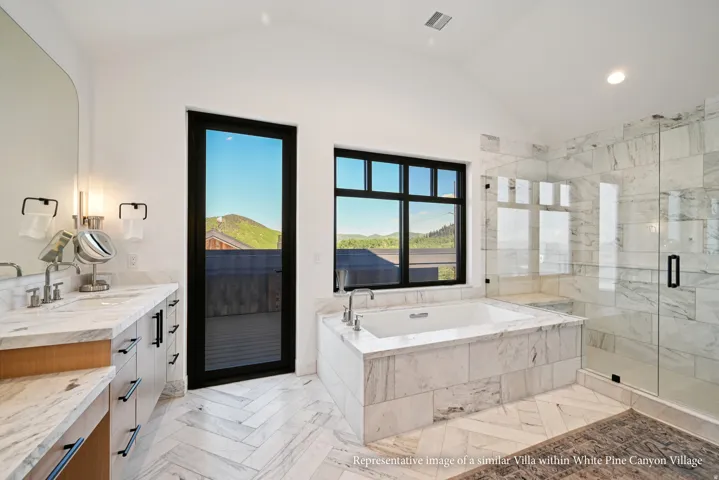 Spacious bathroom featuring a built-in soaking tub, glass-enclosed shower with a bench, dual vanity with undermount sinks, and stone-tiled flooring in a herringbone pattern