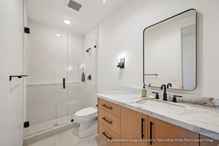 White oak vanity with matte black hardware, stone countertop, undermount sink, and black-framed mirror