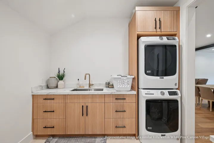 White wood-finish cabinetry with black hardware, undermount sink, and light stone countertop