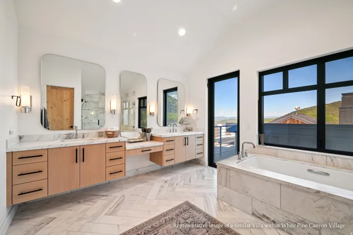 Dual floating vanities with stone countertops, a built-in soaking tub, large format windows, and herringbone pattern tile flooring