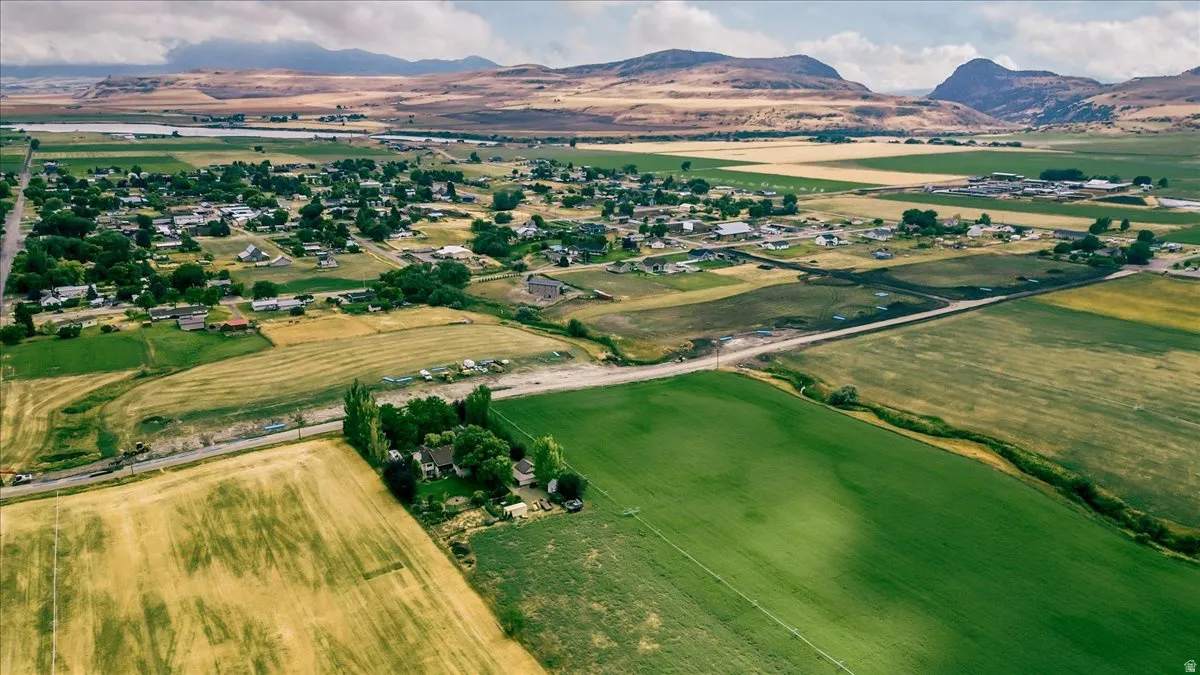Expansive rural landscape featuring a mix of green and golden fields, distant mountains, and a community of homes