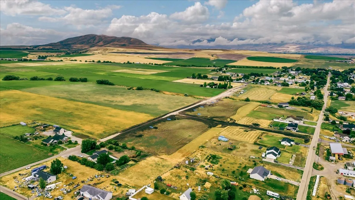 Rural landscape featuring expansive green fields, established residential areas, and distant mountainous terrain