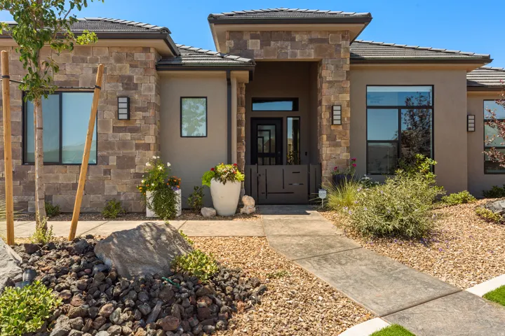 Stone and stucco exterior with multiple large windows, a covered entry, and a stamped concrete walkway
