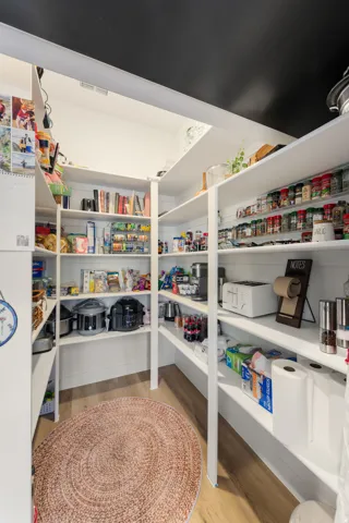 Spacious pantry featuring multiple white built-in shelves and wood-finish flooring