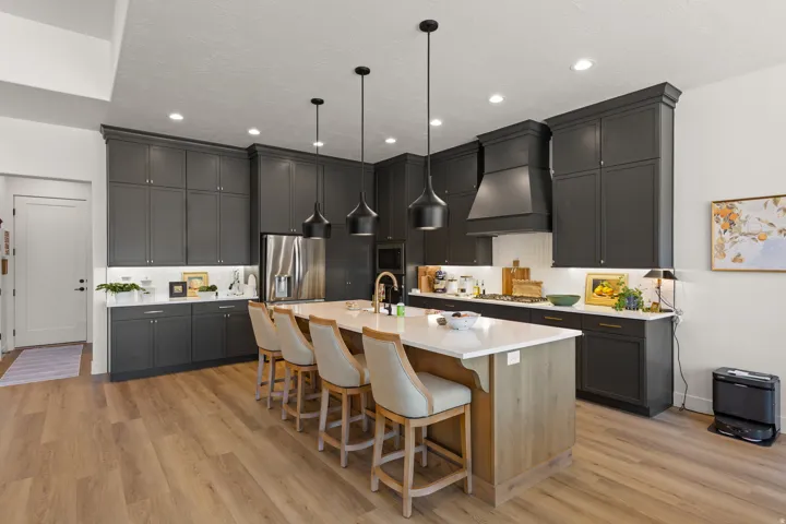 Expansive kitchen featuring wood-finish flooring, dark shaker-style cabinetry, an oversized central island with seating, a professional-grade range hood, and integrated stainless steel appliances