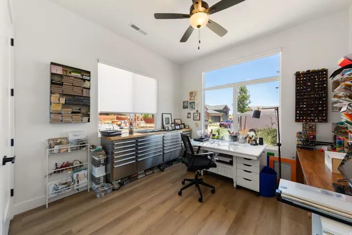 Wood-finish flooring, high ceilings, large windows, ceiling fan with integrated lighting, and white walls