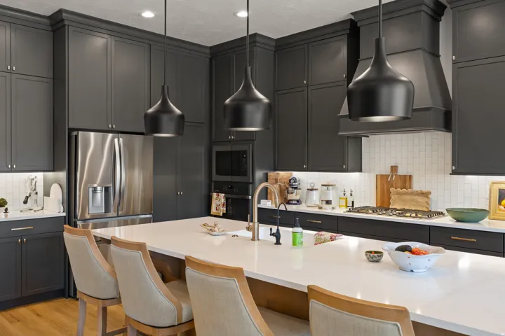 Spacious kitchen featuring dark gray cabinetry, stainless steel appliances, a white subway tile backsplash, a large center island with a sink, and pendant lighting