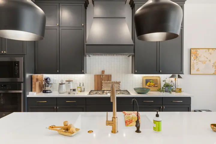 White quartz countertops, dark shaker cabinetry, stainless steel appliances, subway tile backsplash, and a gold-finish kitchen faucet