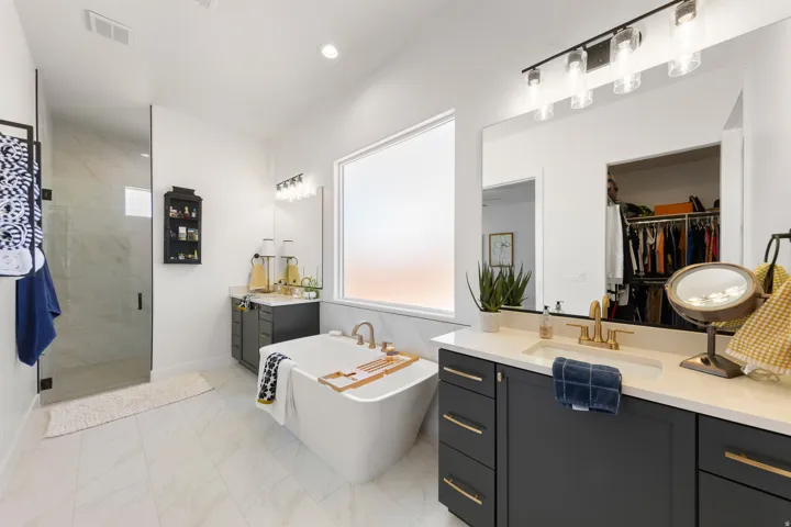 Freestanding soaking tub with gold-finish fixtures, dual vanity with undermount sinks, separate glass-enclosed shower, and built-in closet storage