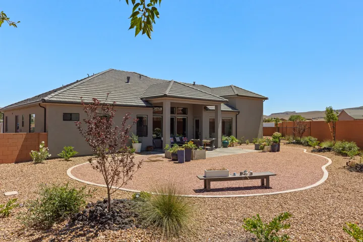Expansive gravel backyard featuring a curved concrete patio, mature landscaping, and stucco exterior