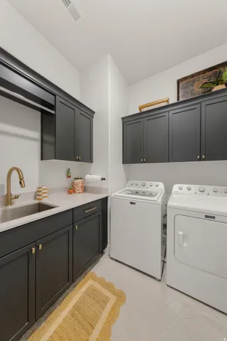 Laundry area featuring dark cabinetry, a built-in sink with a gold-tone faucet, light-toned countertops, and honeycomb tile flooring