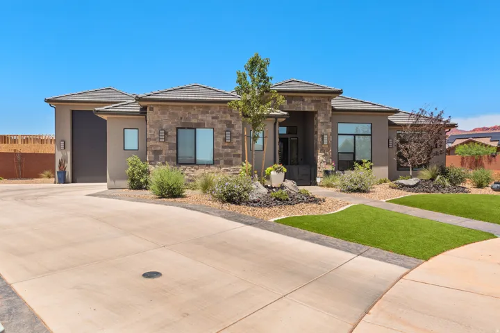 Stone and stucco exterior with dark-frame windows, a tiled roof, and a visible garage door