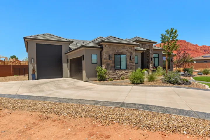 Stucco exterior with stone accents, concrete tile roofing, a two-car garage, and desert landscaping