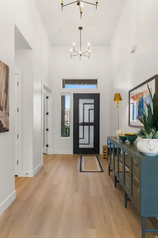 Vaulted entry with wood-finish flooring, a contemporary black entry door, and two chandelier light fixtures