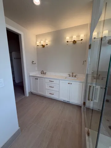 Dual vanity with white cabinetry, integrated sinks, white countertops, and wall-mounted lighting fixtures