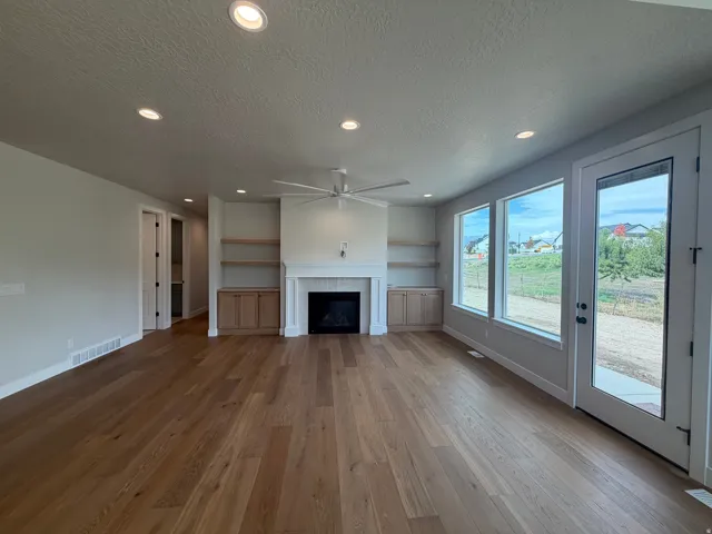 Spacious room featuring wood-finish flooring, a built-in fireplace with a hearth, recessed lighting, and large windows with a door leading outside