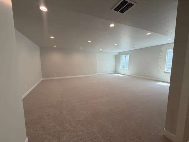 Spacious room with recessed lighting, light-toned carpeting, multiple windows with white blinds, and white trim