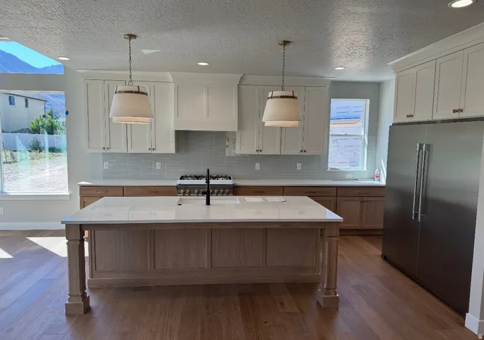 Gourmet kitchen with a large center island, stainless steel refrigerator, white upper cabinetry, natural wood lower cabinetry, and wood-finish flooring