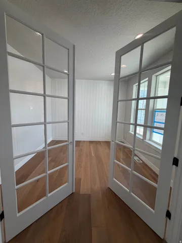 Double French doors with clear glass panels open to a room featuring wood-finish flooring, white shiplap walls, and recessed lighting