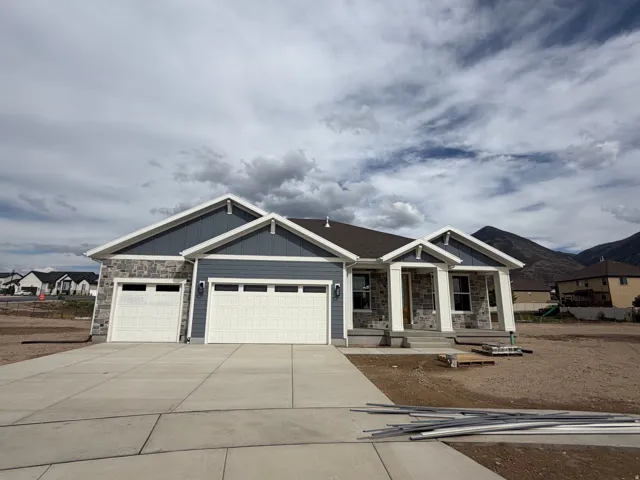 Stone and siding exterior with a covered porch, multiple garages, and a concrete driveway