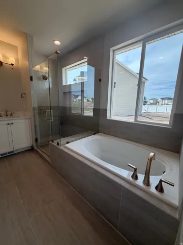 Soaking tub with brushed nickel fixtures, a glass-enclosed shower, a double vanity with white cabinetry, and tile flooring